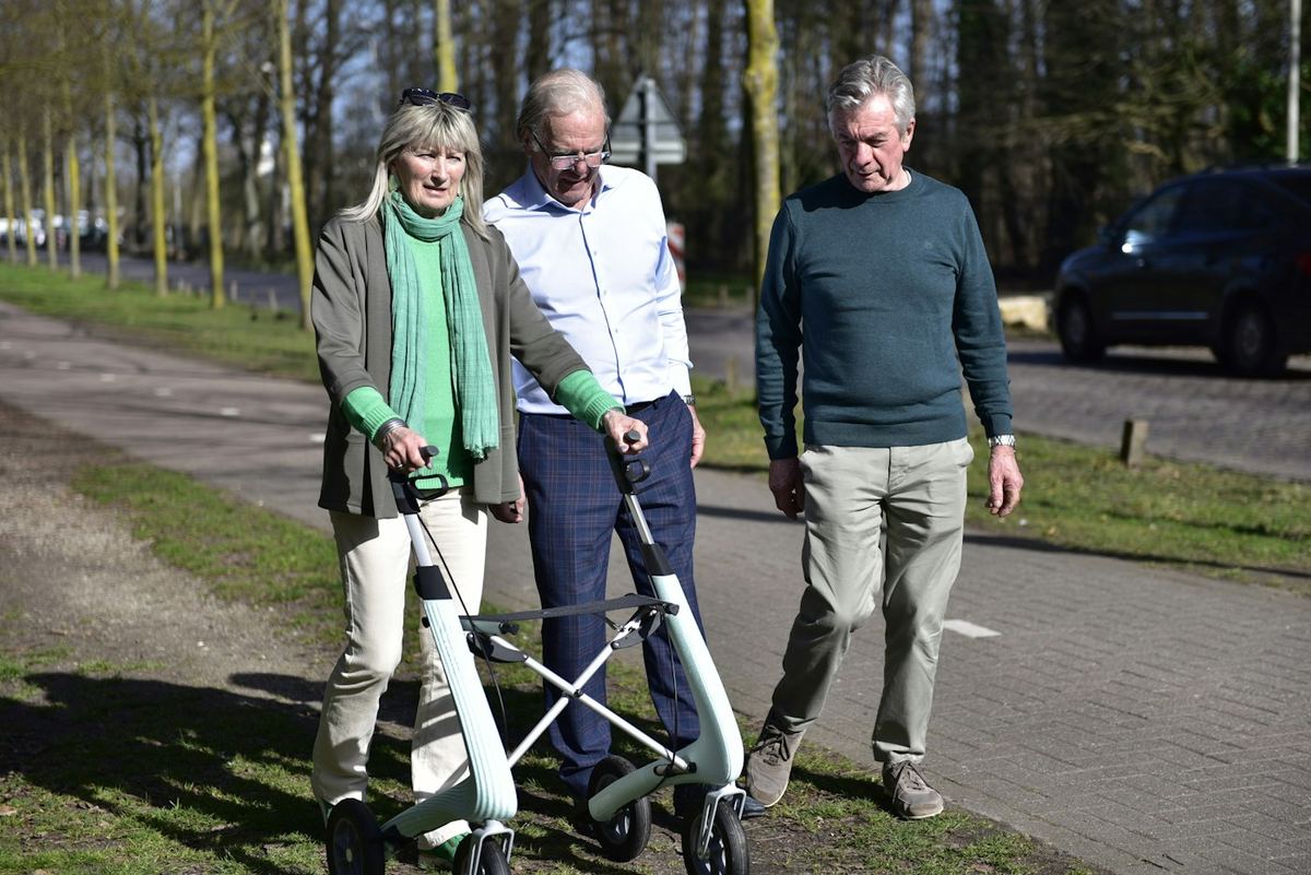 Three people walking together with a walker on a sunny path